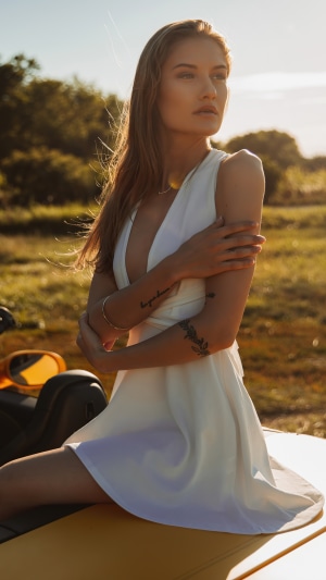 Model in white dress sitting on a yellow vehicle