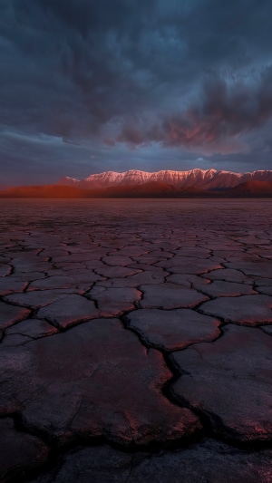 Cracked desert landscape with mountains at sunset