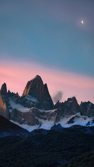Snow-capped mountains under a twilight sky with a crescent moon