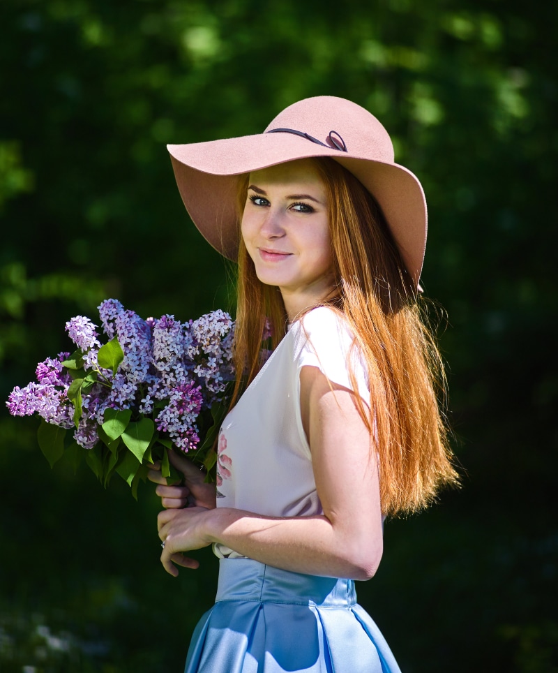 Redhead girl with lilac bouquet wearing a hat
