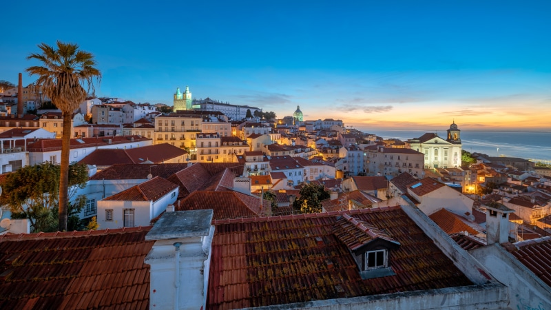 Lisbon, Portugal cityscape with palm trees and ocean at dusk
