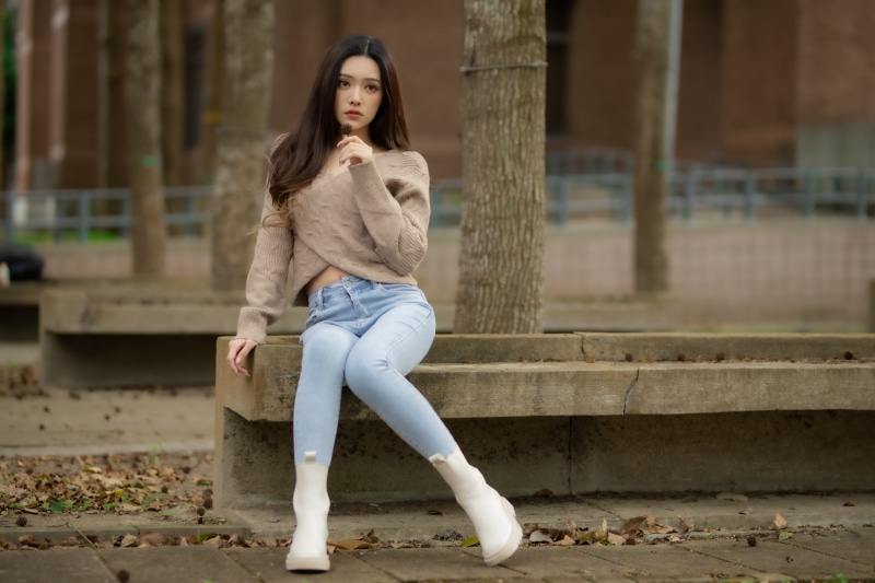 Asian woman sitting on a bench wearing jeans and a sweater