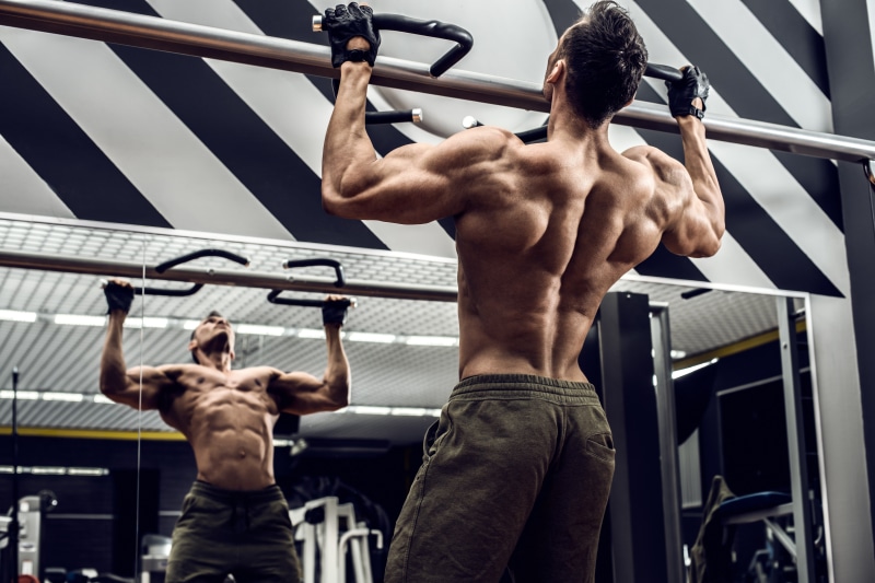 Man doing pull-ups in a gym with mirror reflection