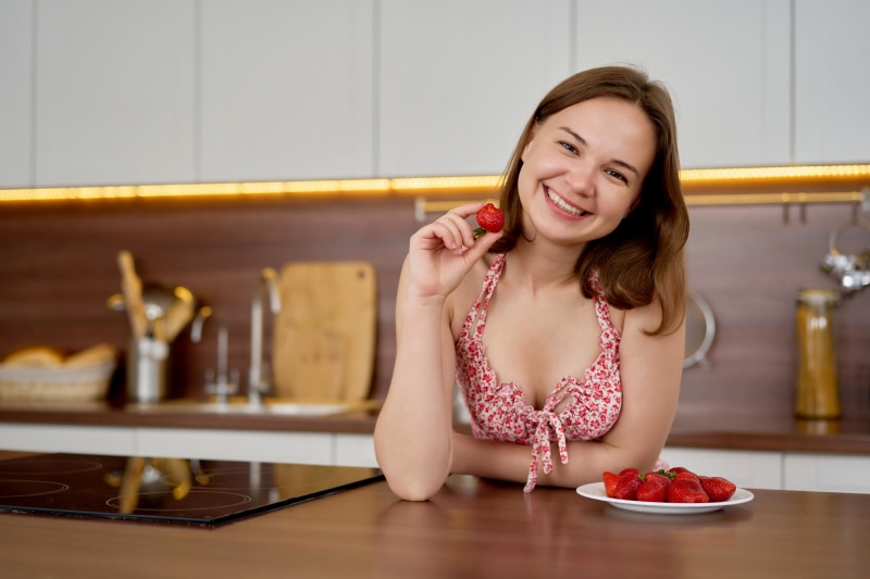 Woman holding a strawberry in a kitchen