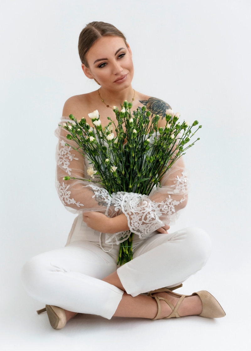 Woman in white sitting with bouquet of flowers