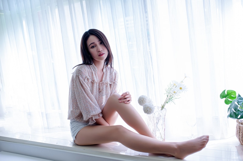 Asian woman sitting by window with flowers