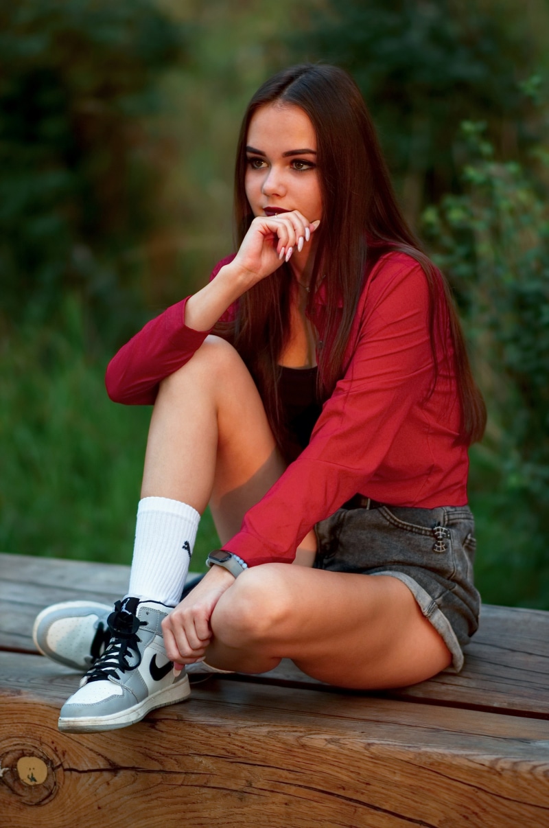Young woman in red blouse and denim shorts sitting outdoors