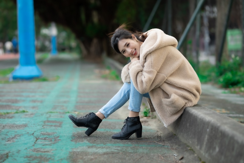 Woman in Fur Coat and Jeans Sitting Outdoors