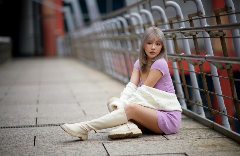 Asian woman wearing a purple dress and white boots sitting on a walkway