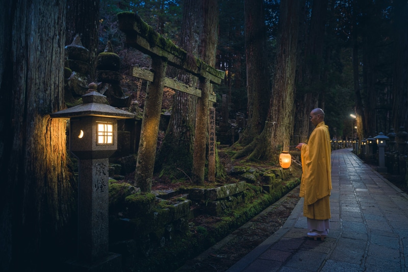 Monk holding lantern in Japanese forest at dusk