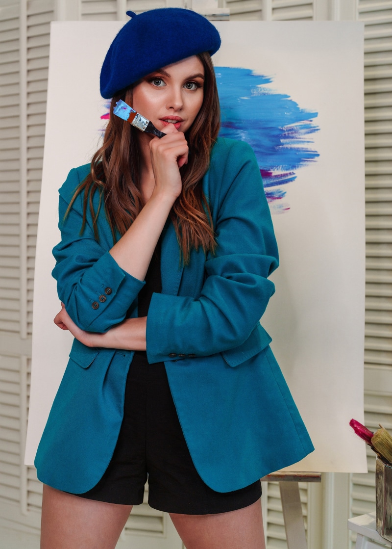 Woman in blue beret and teal jacket holding paintbrush