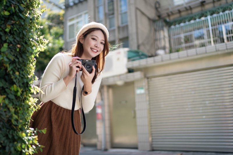 Asian woman in beret and sweater holding camera