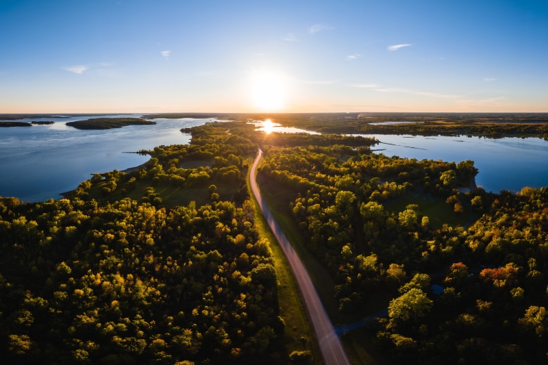 Aerial view of a road through a forest by a lake at sunset