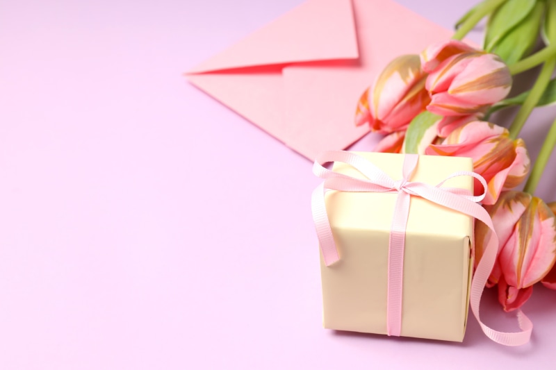 Gift box with pink tulips and envelope on pink background