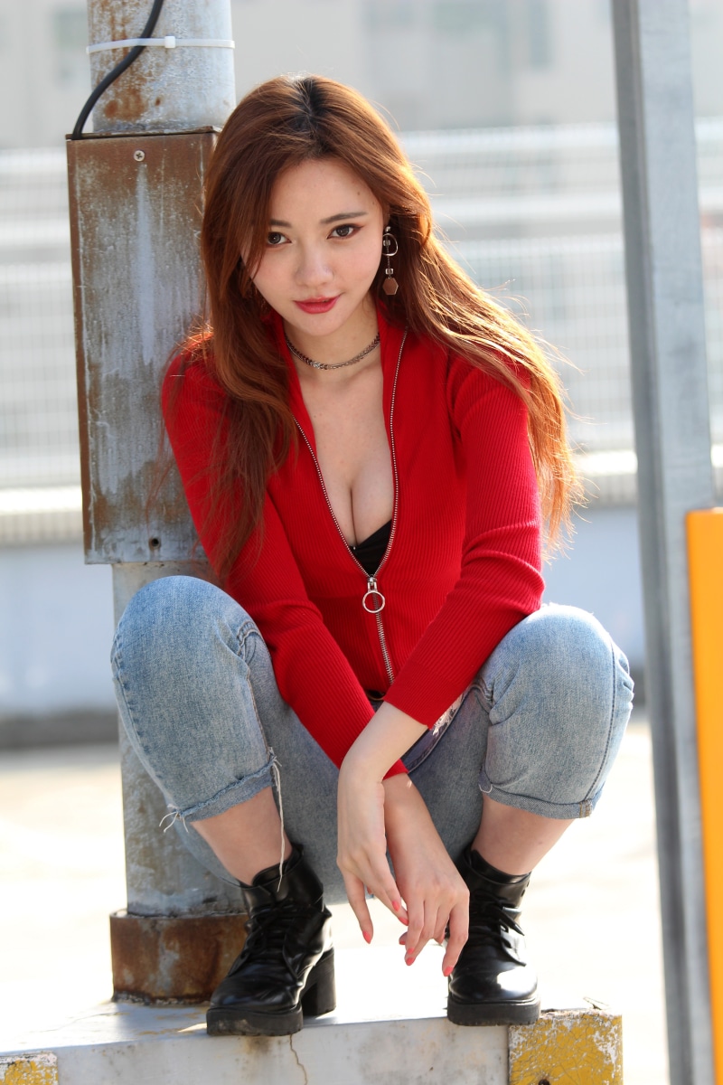 Asian woman in red jacket and jeans posing outdoors