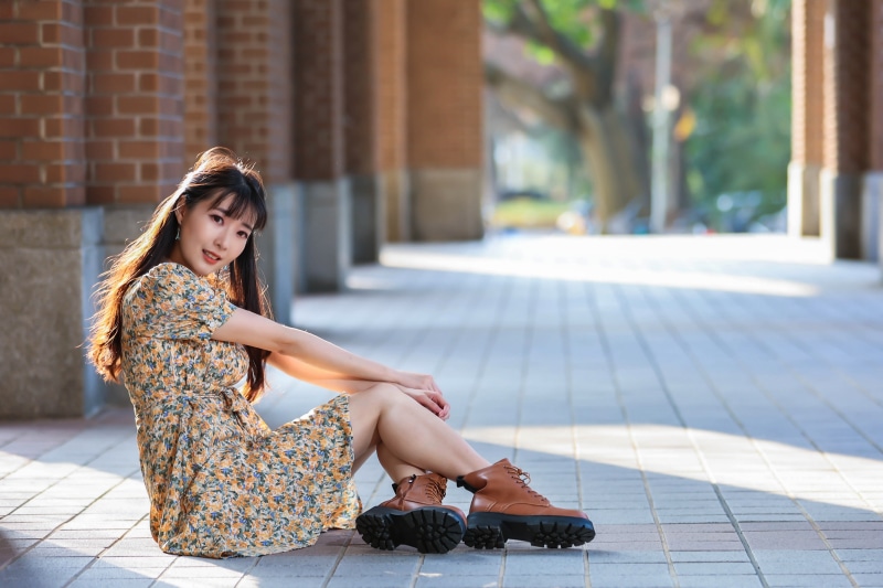 Asian woman sitting outdoors in a floral dress and boots