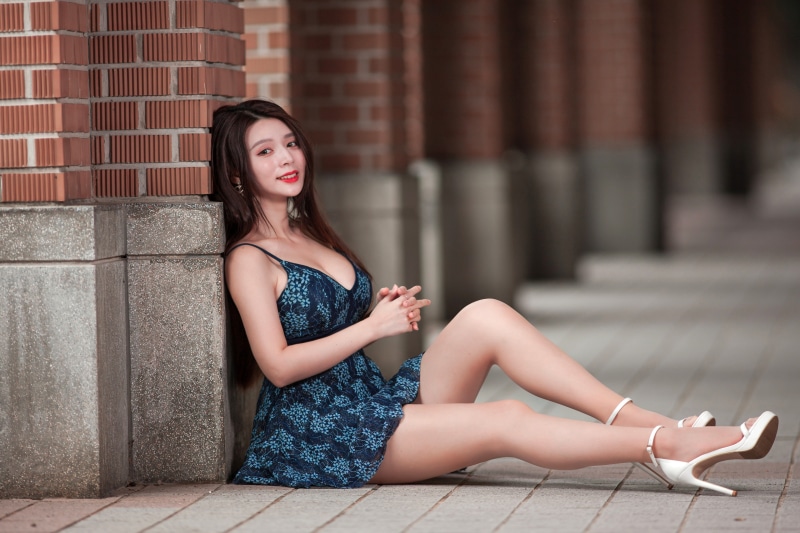 Asian woman in blue dress sitting by brick wall