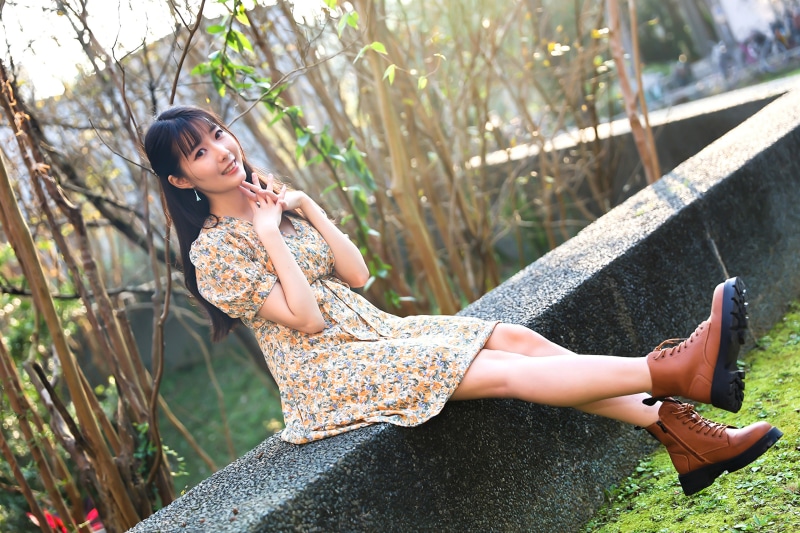 Asian woman in floral dress and boots sitting outdoors