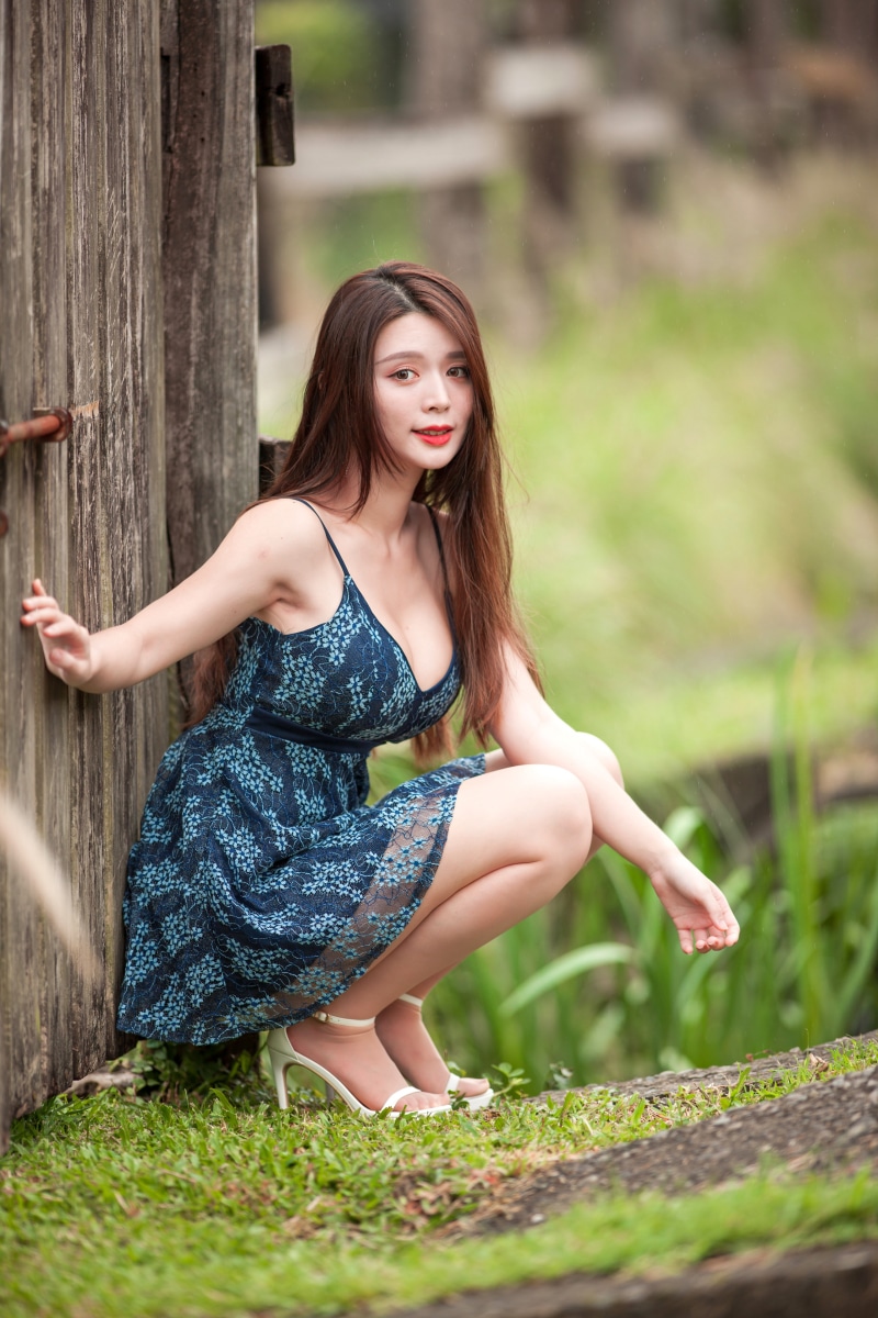 Asian woman in blue dress crouching by wooden post