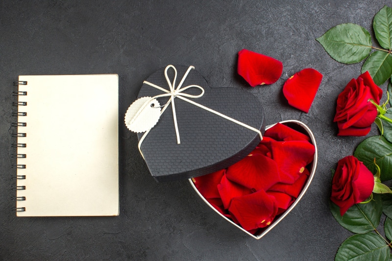 Heart-shaped gift box with roses and petals next to a notepad