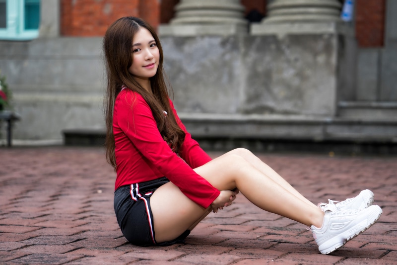 Asian woman sitting on brick ground wearing red shirt and shorts