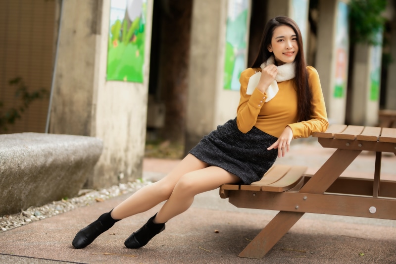 Asian woman sitting on a bench wearing a skirt and sweater