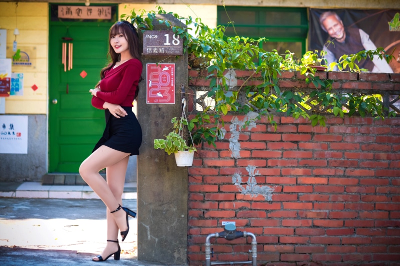 Asian woman in red blouse and black skirt posing outdoors