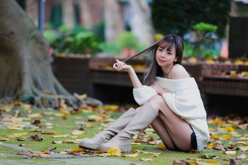Asian woman sitting on the ground wearing boots and sweater