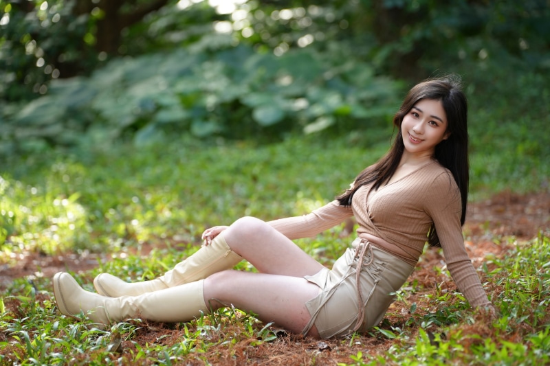Asian woman sitting in a park wearing boots and skirt