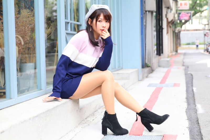 Asian woman in beret and sweater dress sitting on ledge
