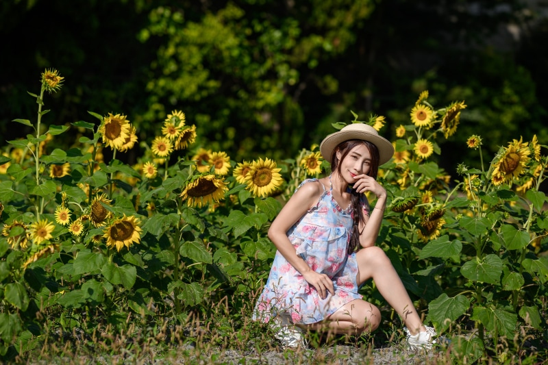 Asian woman in a dress and hat posing in a sunflower field