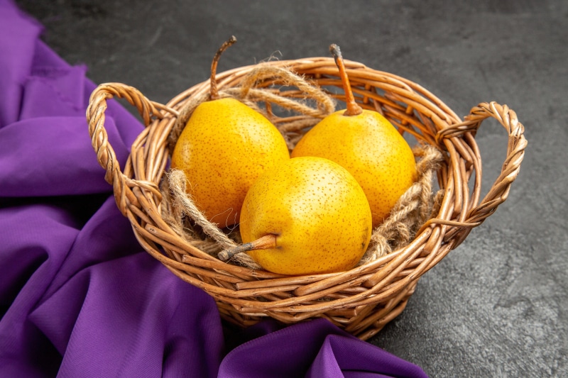 Three yellow pears in a wicker basket with purple cloth