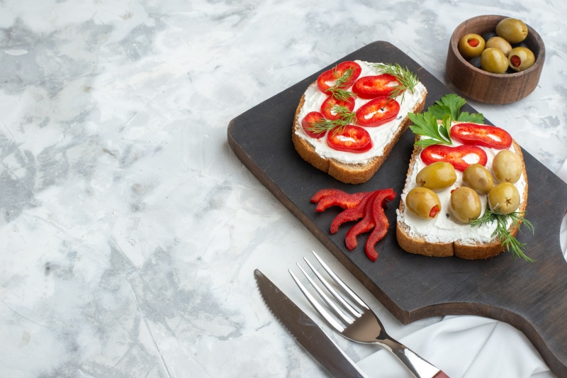 Open-faced sandwiches with olives and bell peppers on a cutting board