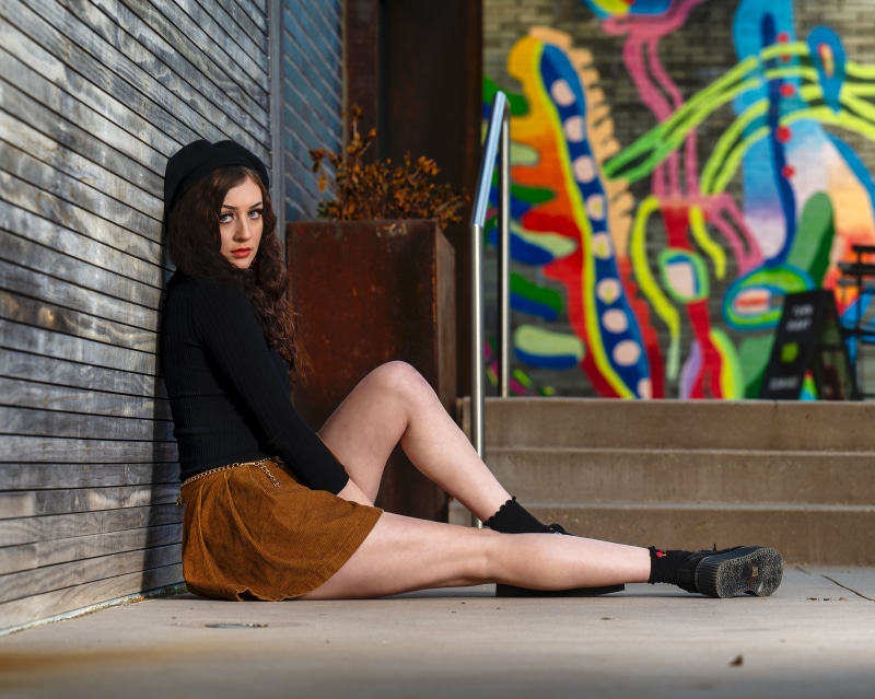 Woman in Beret and Skirt Sitting by Mural