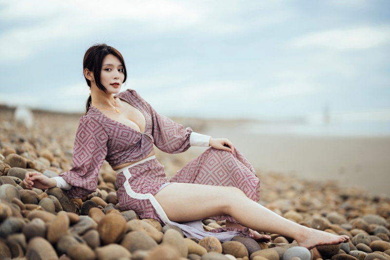 Asian woman in blouse and skirt sitting on stones at beach