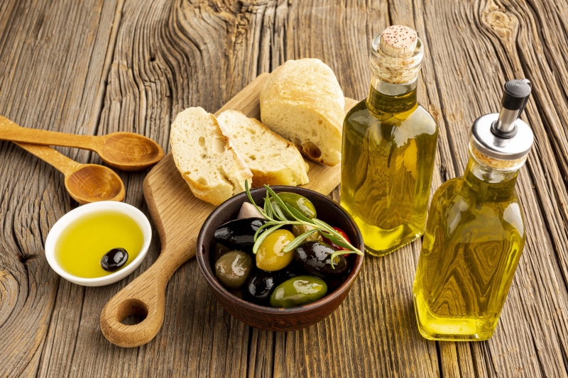 Olive oil, olives, bread, and spoons on a wooden table