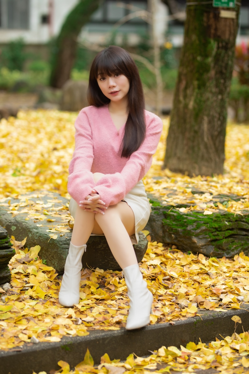 Asian woman sitting on rocks surrounded by autumn foliage