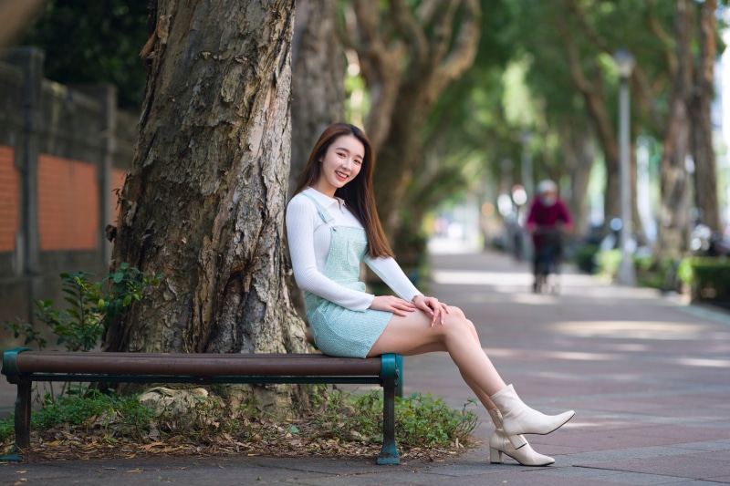 Asian woman sitting on a bench near a tree