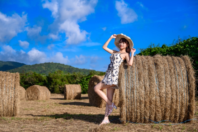 Asian woman in dress and hat posing by hay bales