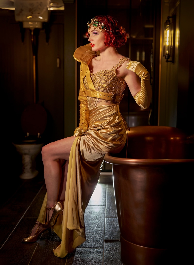 Woman in gold dress and gloves sitting by tub