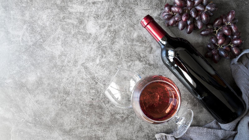 Red wine bottle, glass, and grapes on a textured surface