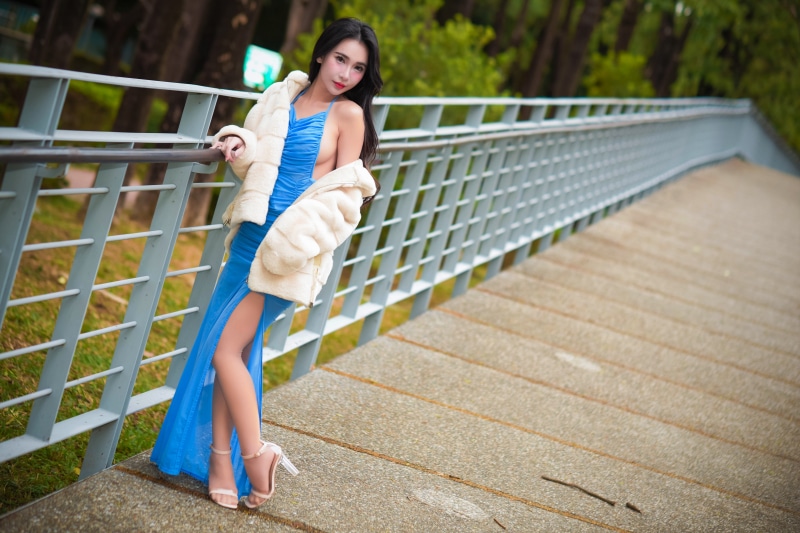 Asian woman in blue dress and fur coat on bridge