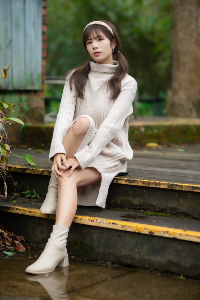 Asian woman in a cream sweater dress sitting on steps