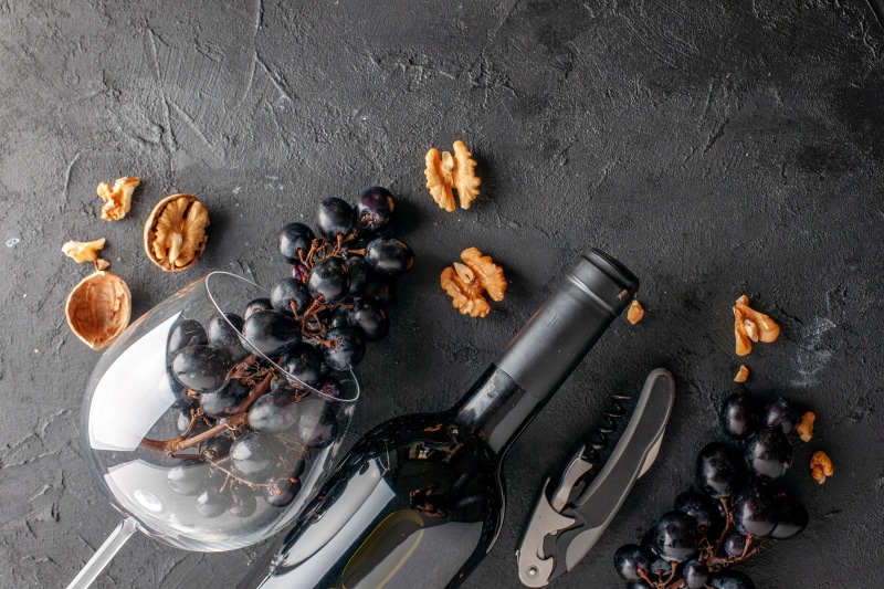 Wine bottle, grapes, walnuts, and corkscrew on dark surface
