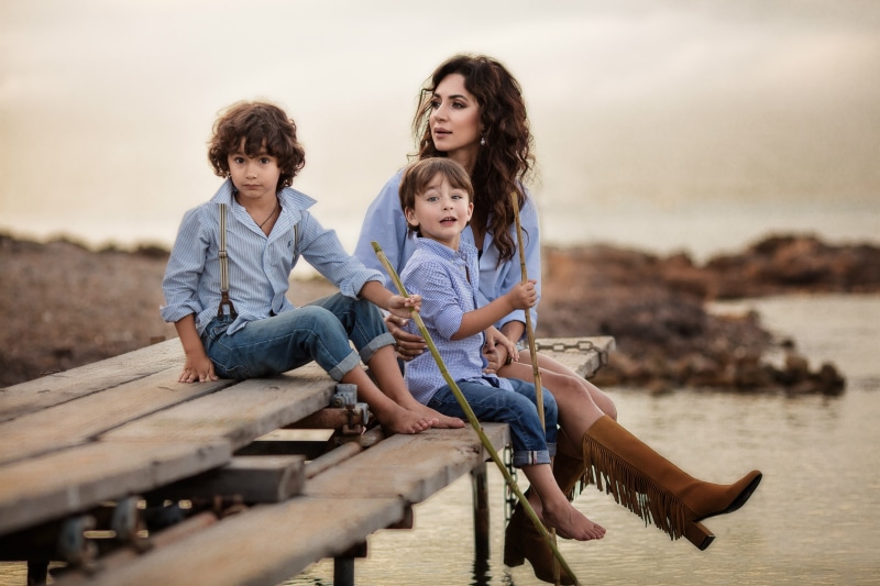 Mother and two sons sitting on a wooden pier