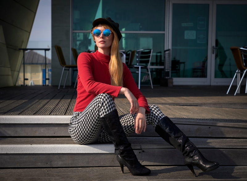 Blonde girl wearing sweater, trousers, boots, cap, and glasses