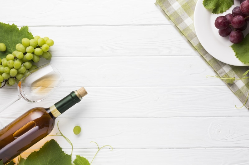 White wooden table with grapes, wine bottle, and glass