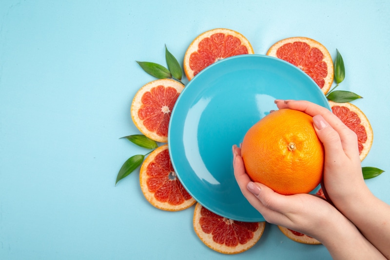 Hands holding orange with grapefruit slices on blue background
