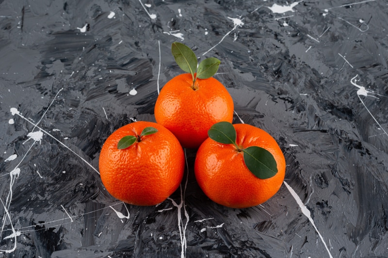 Three Mandarins with Leaves on Textured Surface