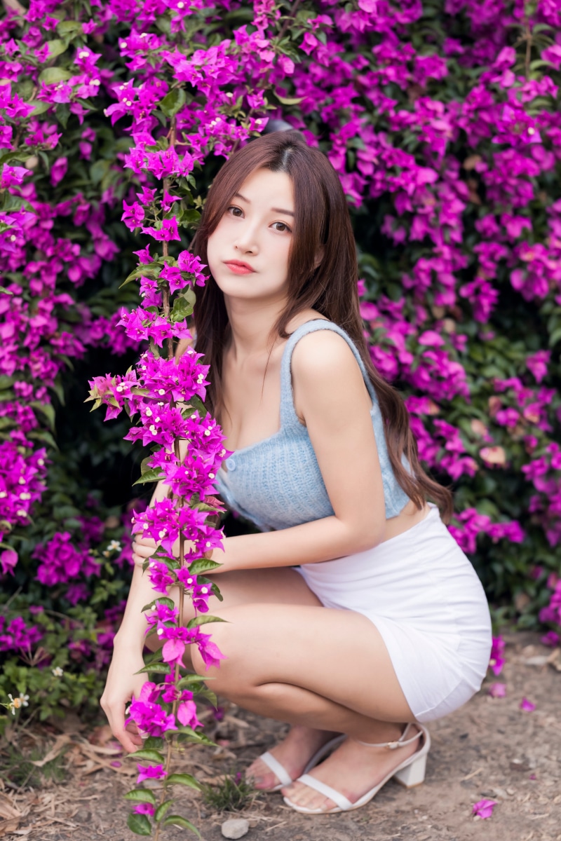 Asian woman in blue top and white skirt posing near purple flowers
